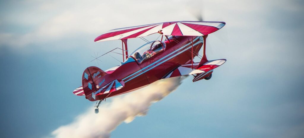 Pitts rouge et blanc en vol avec des fumigène